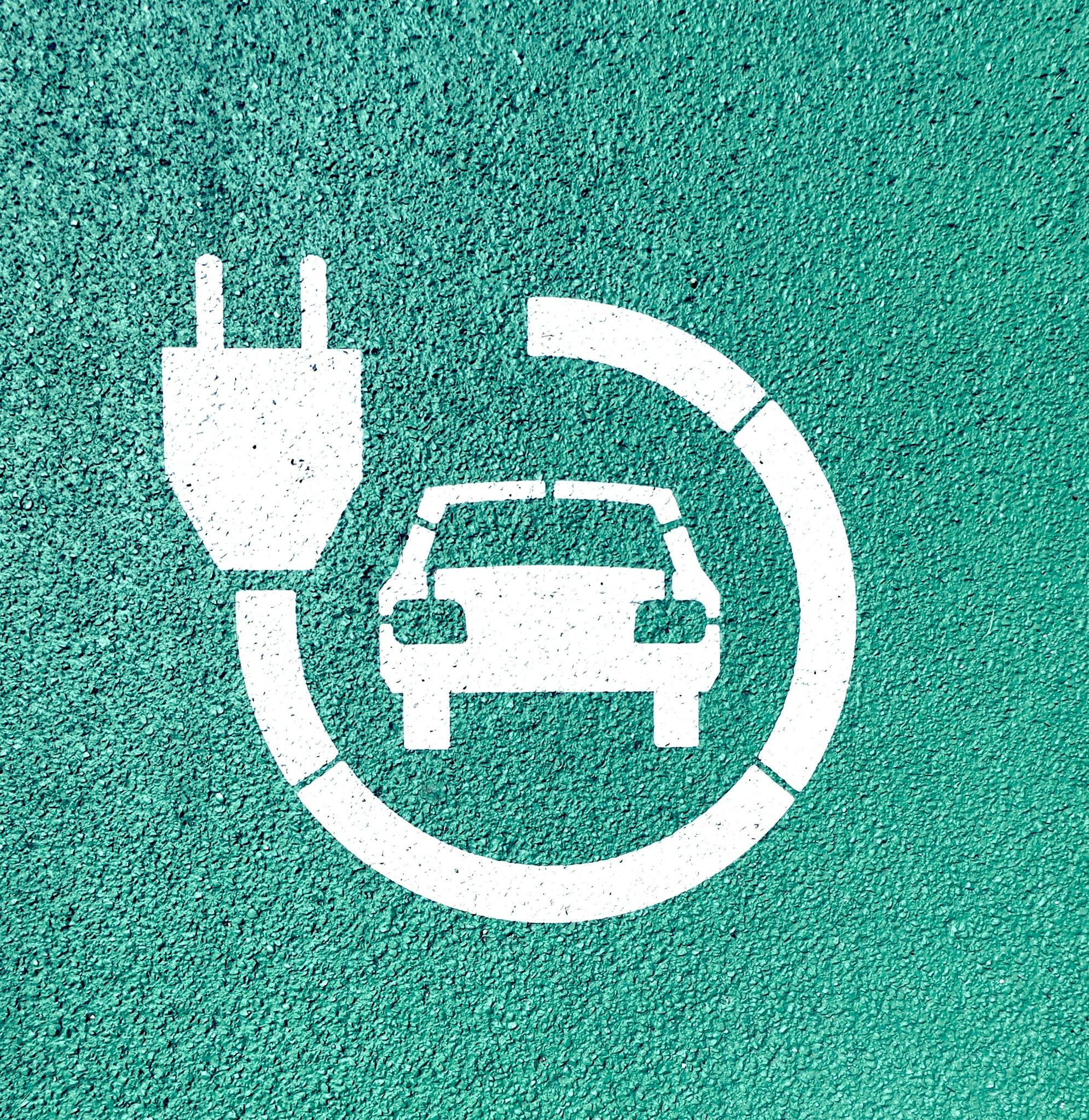 White electric vehicle charging symbol on textured green asphalt background.